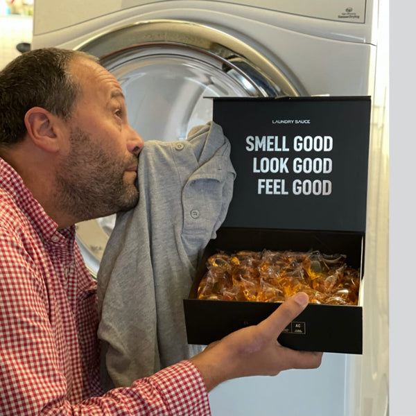 Person smelling a shirt while holding a box of laundry sauce pods